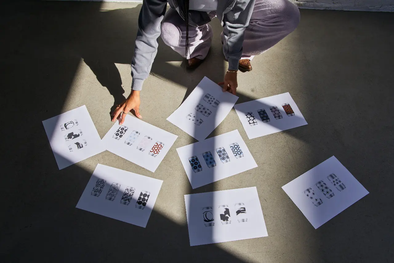 Person arranging multiple printed design options on the floor